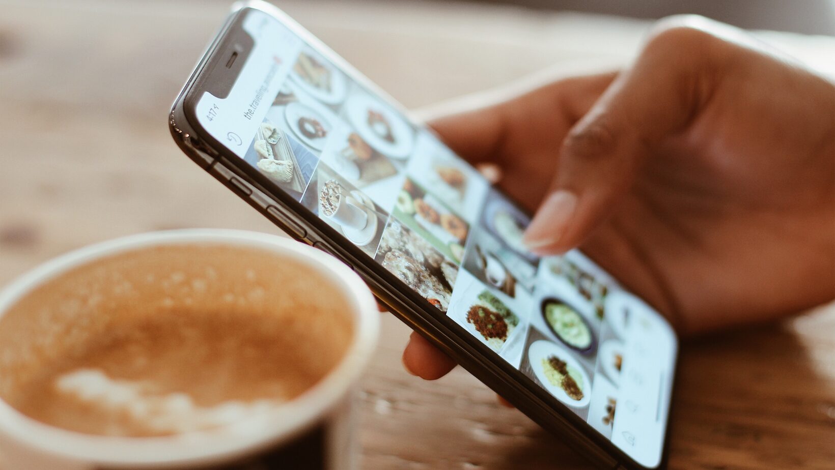 Person with phone in hand displaying the Instagram app next to a cup of coffee.